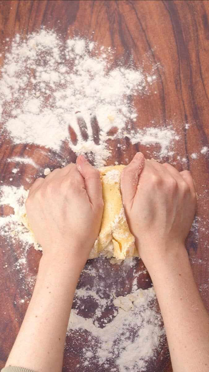 Two hands kneading a round of pie dough inorder to mix the incredients and to make it pliable. Hostess At Heart