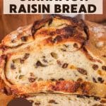 An image for Pinterest of a golden brown sourdough cinnamon raisin bread with visible raisins and cinnamon swirls, cooling on a cutting board. Hostess At Heart