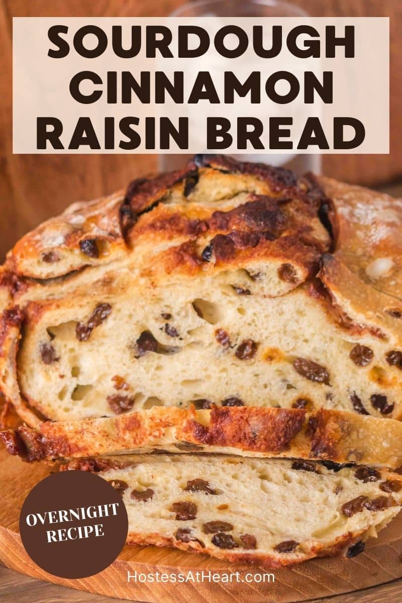 An image for Pinterest of a golden brown sourdough cinnamon raisin bread with visible raisins and cinnamon swirls, cooling on a cutting board. Hostess At Heart