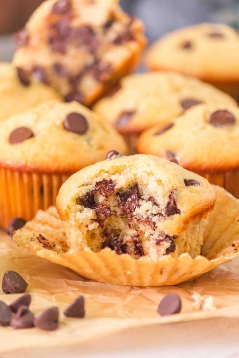 Sideview of a bakery-style chocolate chip sourdough muffin with a bite taken out of it showing a soft crumb filled with melted chocolate chips. Hostess At Heart