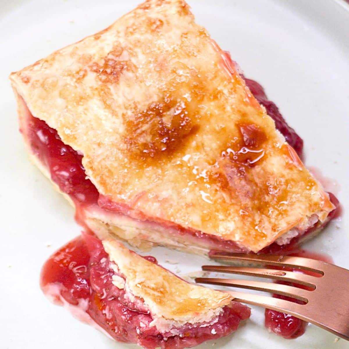 A fork that's cut a piece of homemade strawberry slab pie showing a juicy filling under a golden brown pie crust - Hostess At Heart