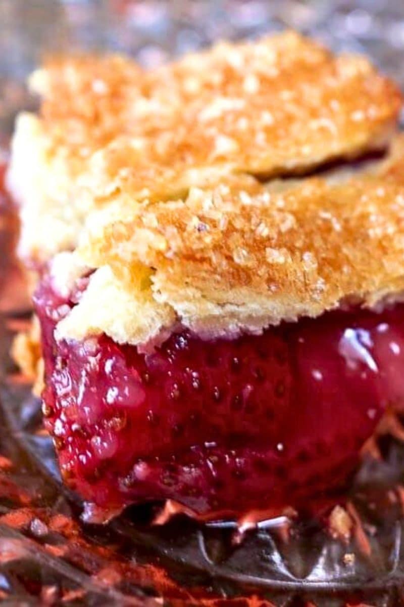 Close up view of a slice of homemade strawberry slab pie showing a bright thick strawberry filling under a golden brown crust. Hostess At Heart