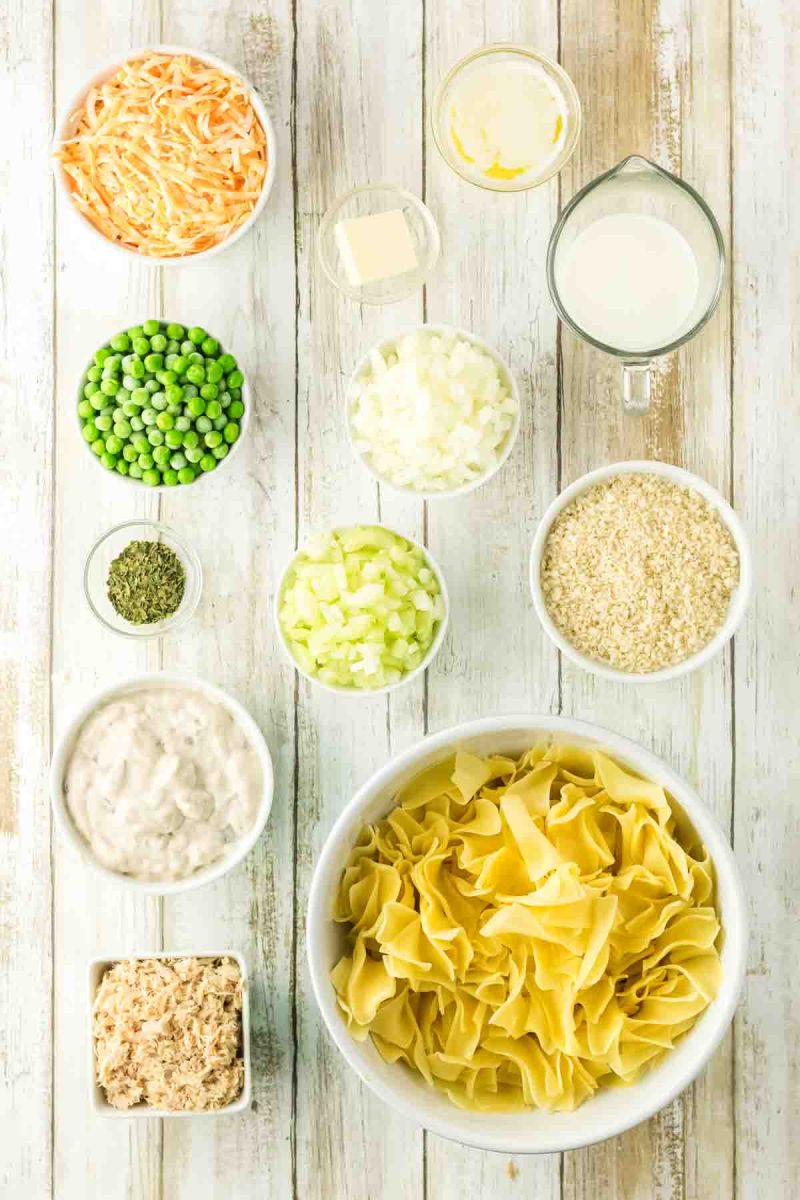 Ingredients used to make a tuna noodle casserole recipe: egg noodles, tuna, cream of mushroom soup, butter, panko bread crumbs, dried parsley, celery, onion, peas, cheese, and milk - Hostess At Heart