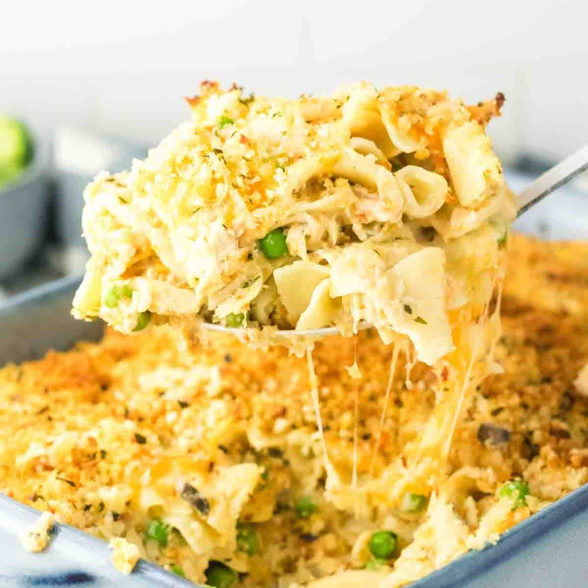 A spatula lifting up a cheesy serving of tuna casserole from the baking dish. Hostess At Heart