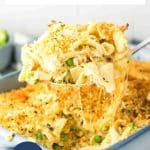 A large spoon lifting a serving of cheesy tuna and noodles casserole from the baking dish showing strings of melted cheese. Hostess At Heart