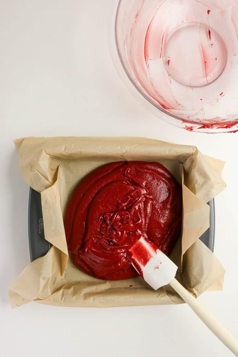 Bright Red Brownie Recipe batter spread in a parchment paper-lined baking pan preparing to be baked. Hostess At Heart