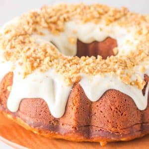 Top down view of a golden brown easy carrot cake topped with a cream cheese glaze garnished with crushed walnuts. Hostess At Heart