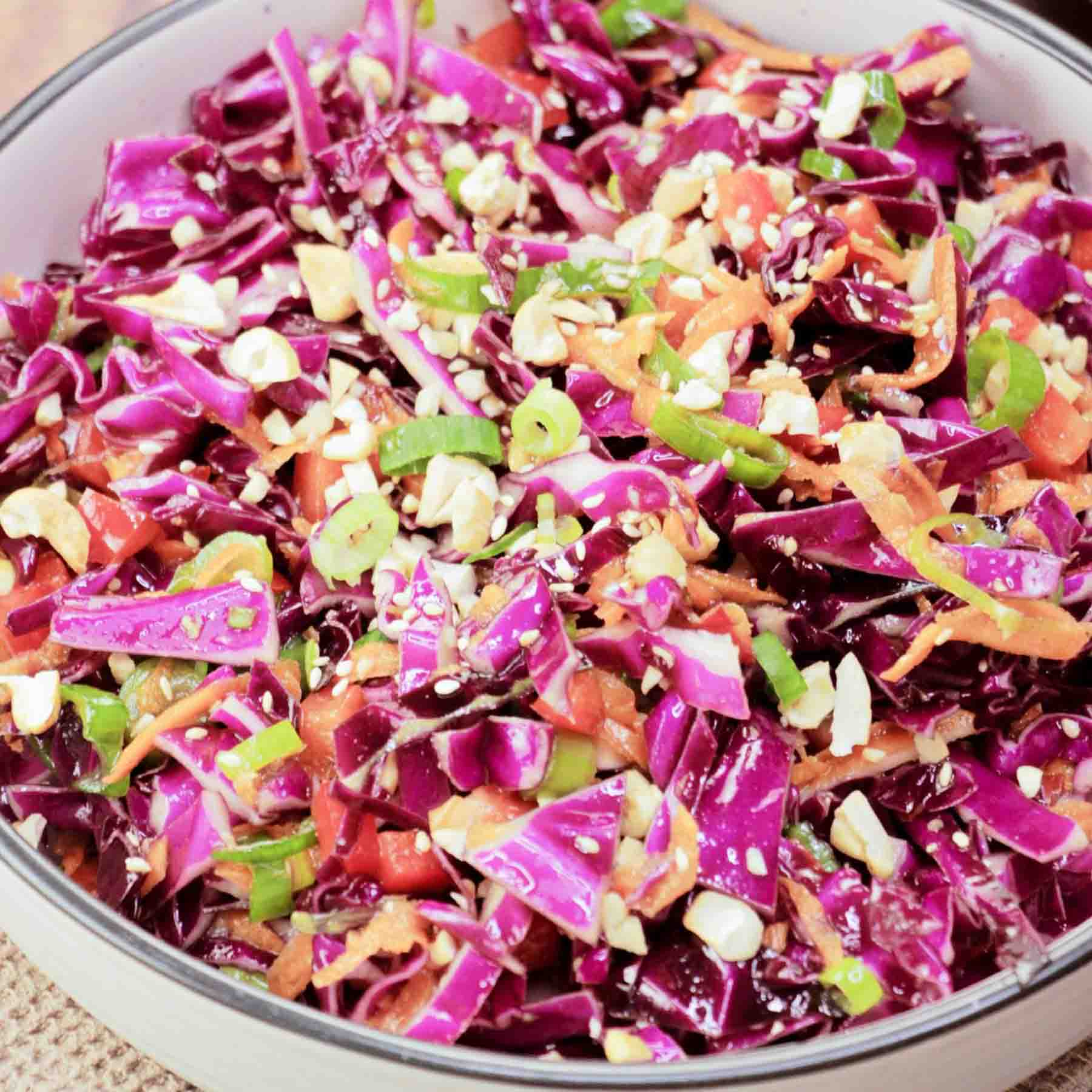 A serving dish filled with an Asian Red Cabbage Salad featuring raw purple cabbage, peppers, carrots, in a ginger dressing garnished with cashews - Hostess At Heart
