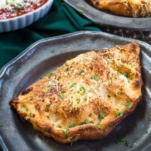 A golden brown baked calzone topped with crispy parmesan fresh from the oven on a metal plate. Hostess At Heart