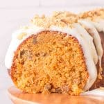 Sliced moist carrot bundt cake on a cake stand showing a tender crumb. It's topped with cream cheese glaze garnished with crushed walnuts - Hostess At Heart