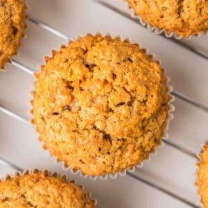 Top down view of golden brown carrot cake muffins sitting on a cooling rack fresh from the oven. Hostess At Heart
