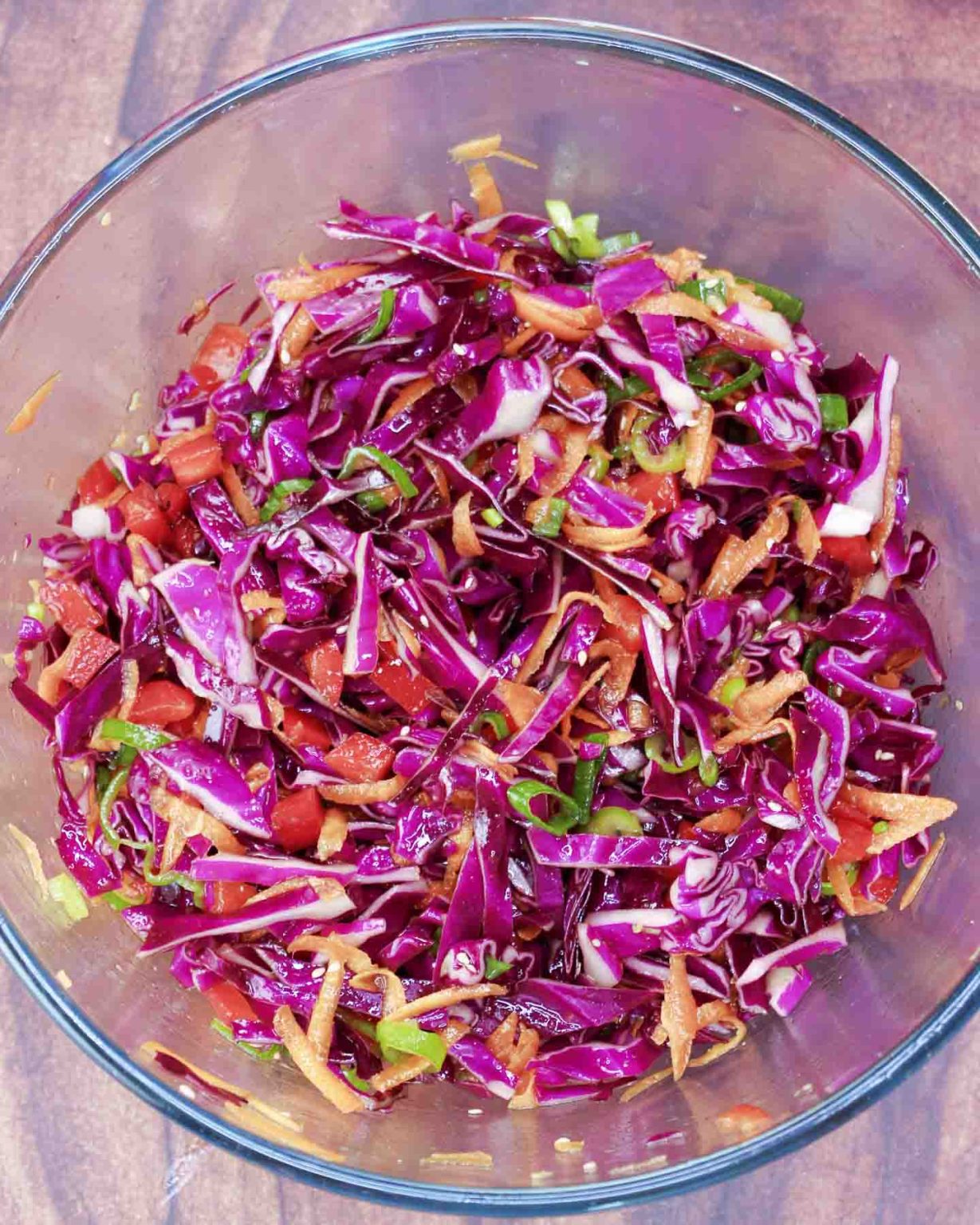 A mixing bowl filled with an Asian Red Cabbage Salad featuring raw purple cabbage, peppers, carrots, that's dressed in a ginger vinaigrette - Hostess At Heart