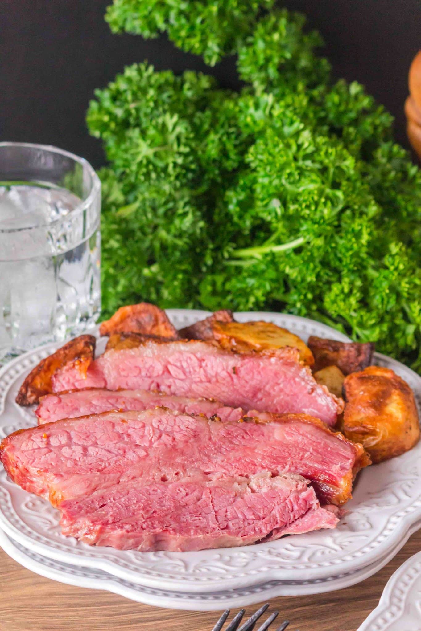 Slices of corned beef brisket fanned out on a serving plate next to some roasted potatoes. Hostess At Heart
