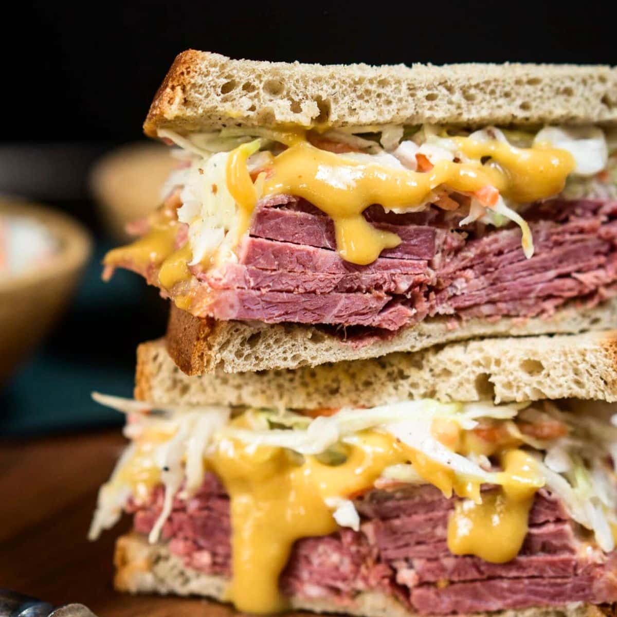 Tableview image of a loaded corned beef sandwich showing layers of sliced corned beef, a mustard sauce, and cabbage slaw on rye bread. Hostess At Heart
