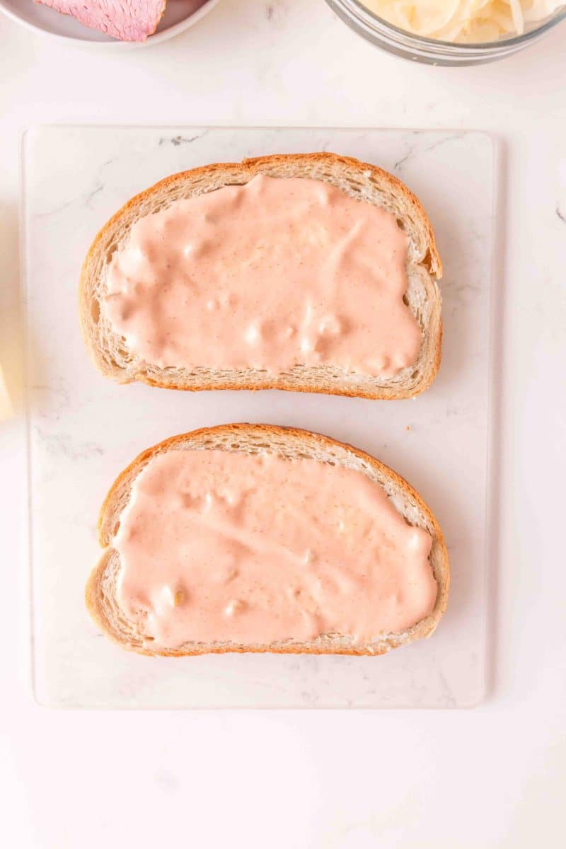Top down view of two slices of rye bread slathered with creamy thousand island dressing. Hostess At Heart