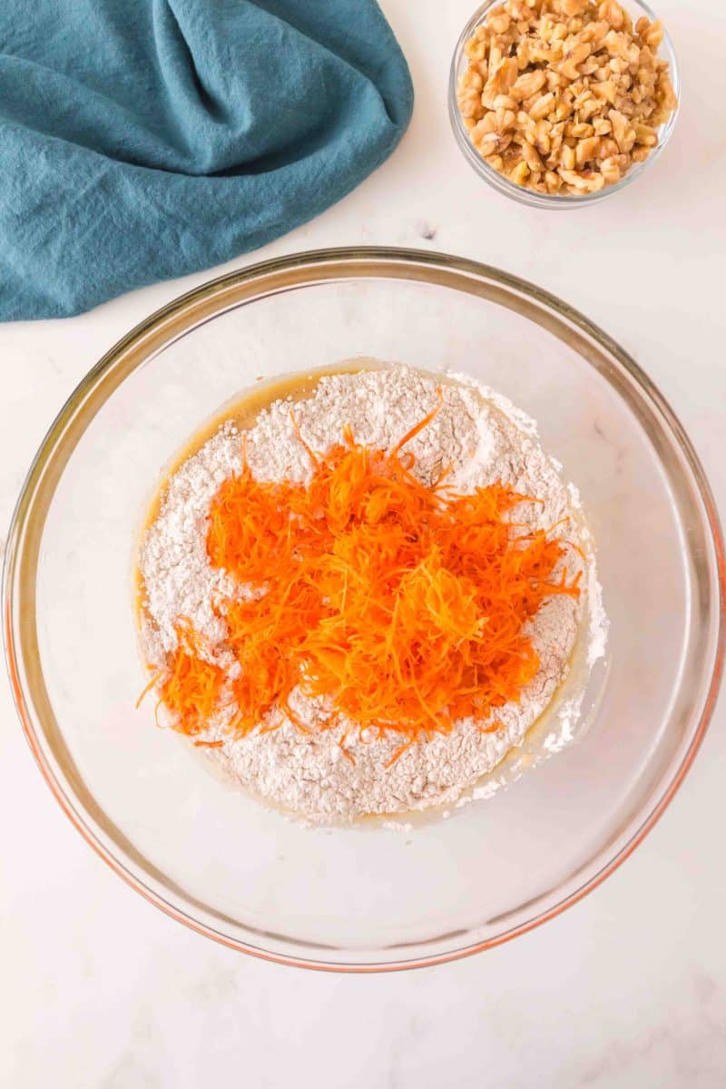 Finely shredded carrots in a mixing bowl filled with homemade carrot cake batter. Hostess At Heart