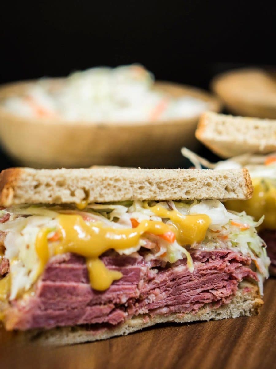 Front view of half of a corned beef sandwich showing layers of moist corned beef, cabbage slaw, and a rich mustard sauce on rye bread. Hostess At Heart