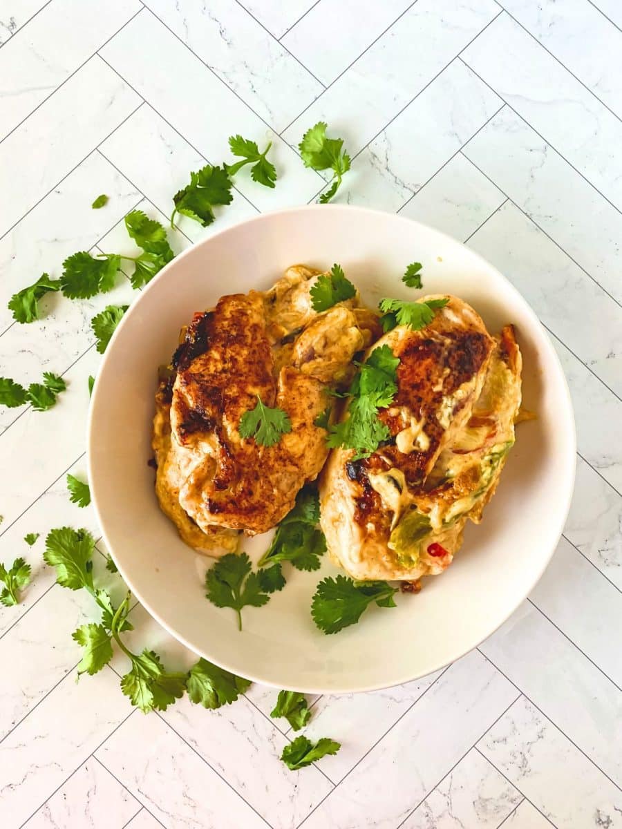 Top down view of two stuffed Gluten-Free chicken breasts baked to a golden brown. Melted cheese and bell peppers are oozing from one of the chicken breasts. Hostess At Heart