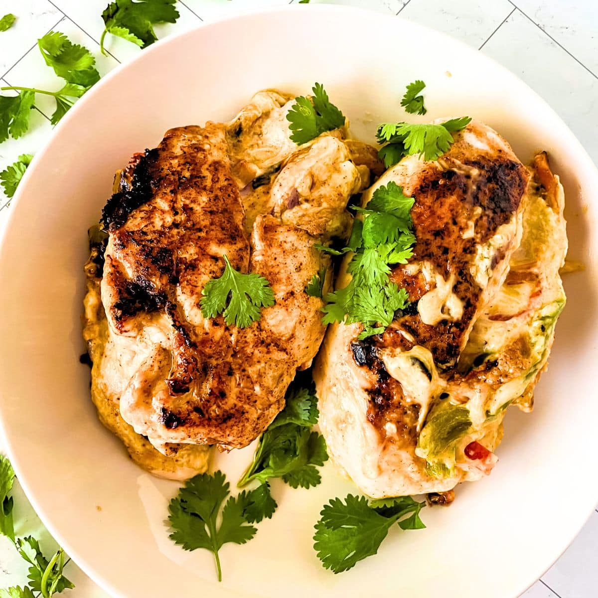 Top down view of a white serving dish filled with two plump golden brown baked stuffed chicken breasts garnished with cilantro. Hostess At Heart