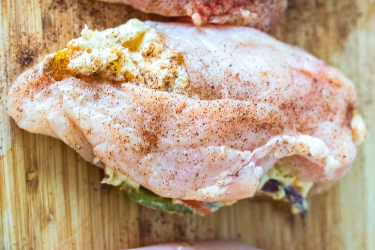 Top down view of a chicken breast sliced and filled with cheesy fajita filling and seasoned with spices ready for baking - Hostess At Heart