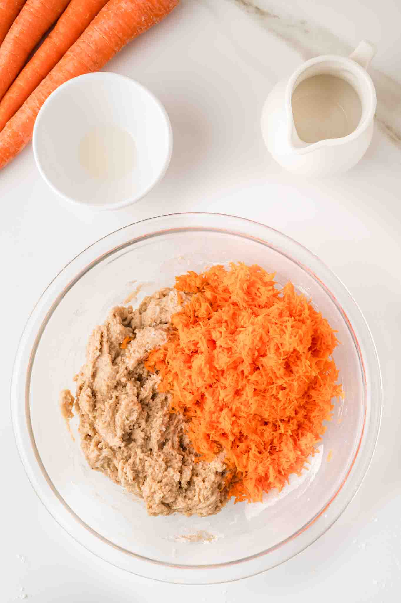 A large mixing bowl filled with carrot cake muffin batter topped with shredded carrots. Hostess At Heart
