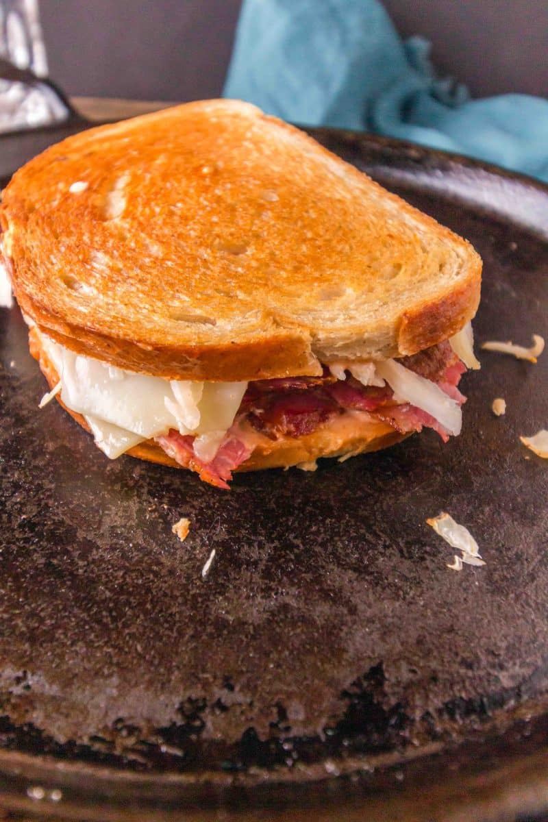A grilled corn beef reuben sandwich cooking on a blacktop pan. Hostess At Heart