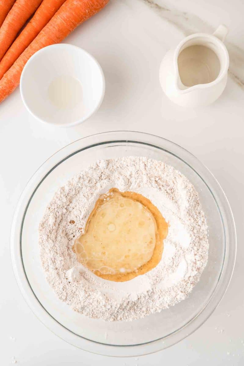 A mixing bowl filled with dry ingredients for carrot muffins with a well shaped and filled with carrot cake wet ingredients ready to be folded together. Hostess At Heart