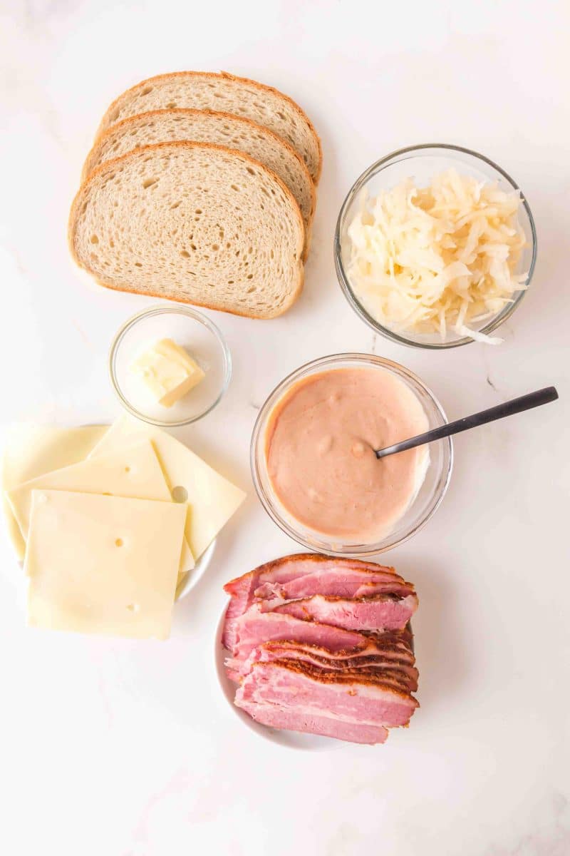 Ingredients for what is a reuben sandwich including sliced corned beef, sauerkraut, homemade thousand island dressing, butter, Swiss Cheese, and slices of rye bread. Hostess At Heart