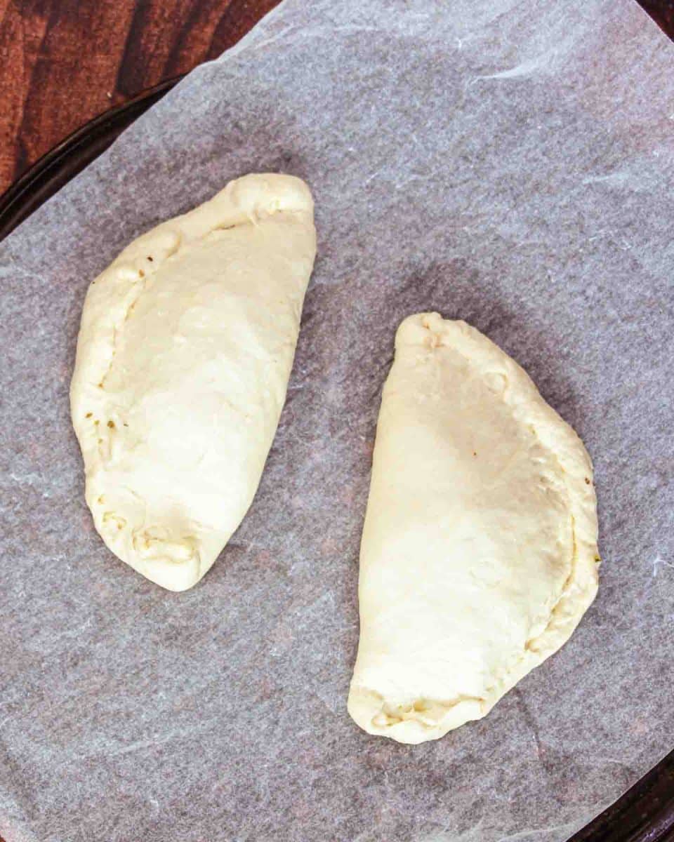 Sealed calzone on a parchment paper-lined baking sheet. Hostess At Heart