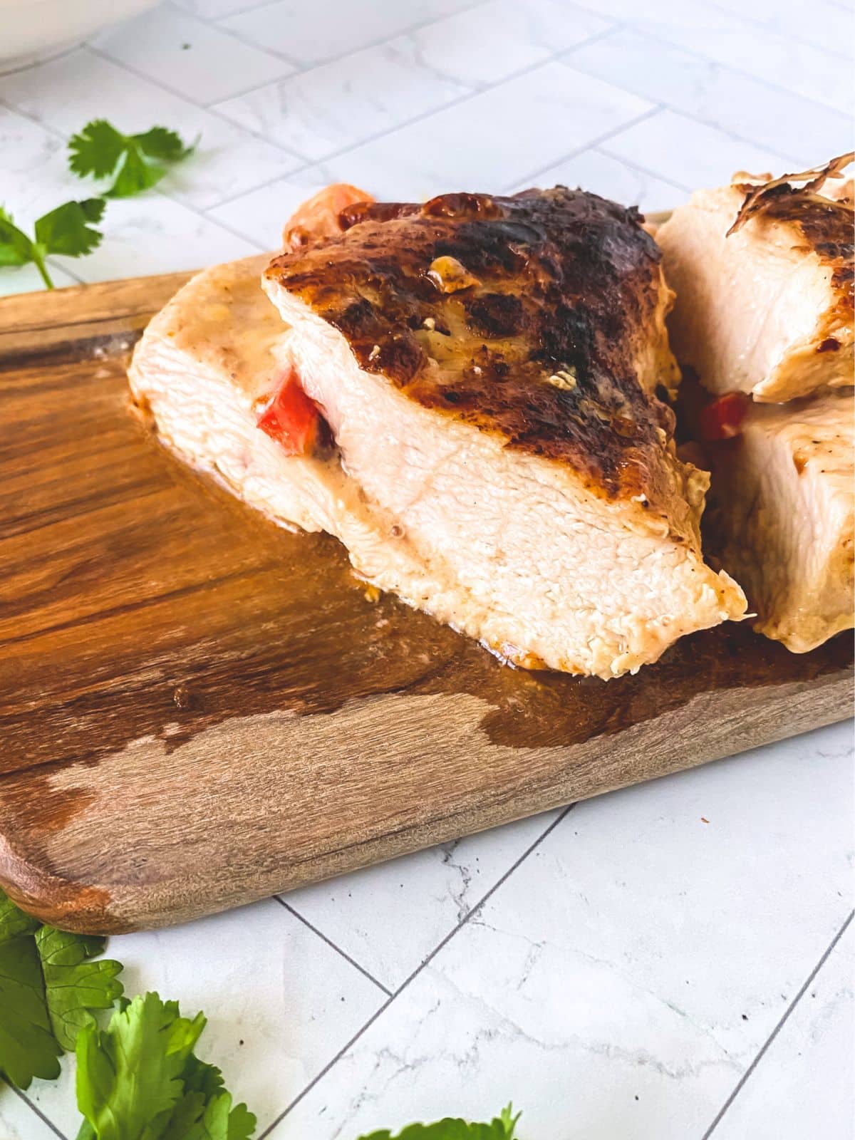 Closeup view of a cutting board topped with a sliced baked stuffed chicken breast showing a tender juicy center filled with fajita cheese and peppers. Hostess At Heart
