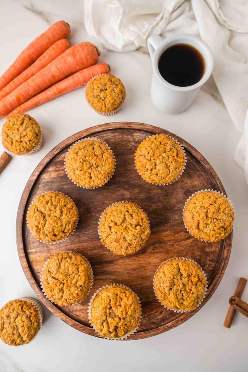 Top down view of freshly baked moist carrot cake muffins on a round wooden serving platter. - Hostess At Heart