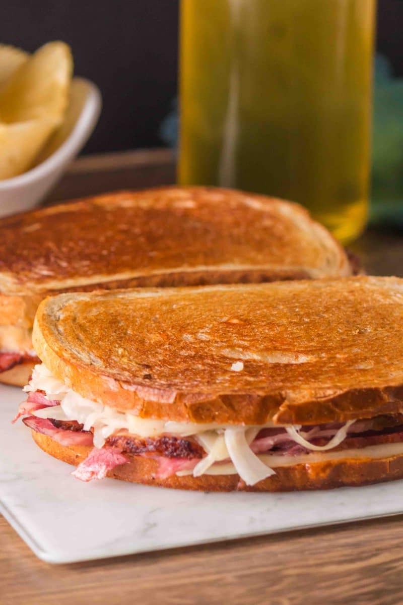 Two grilled leftover corned beef Reuben sandwiches sitting on a marble cutting board. Slices of corned beef, sauerkraut, and Swiss Cheese shows between the two slices of rye bread. Hostess At Heart