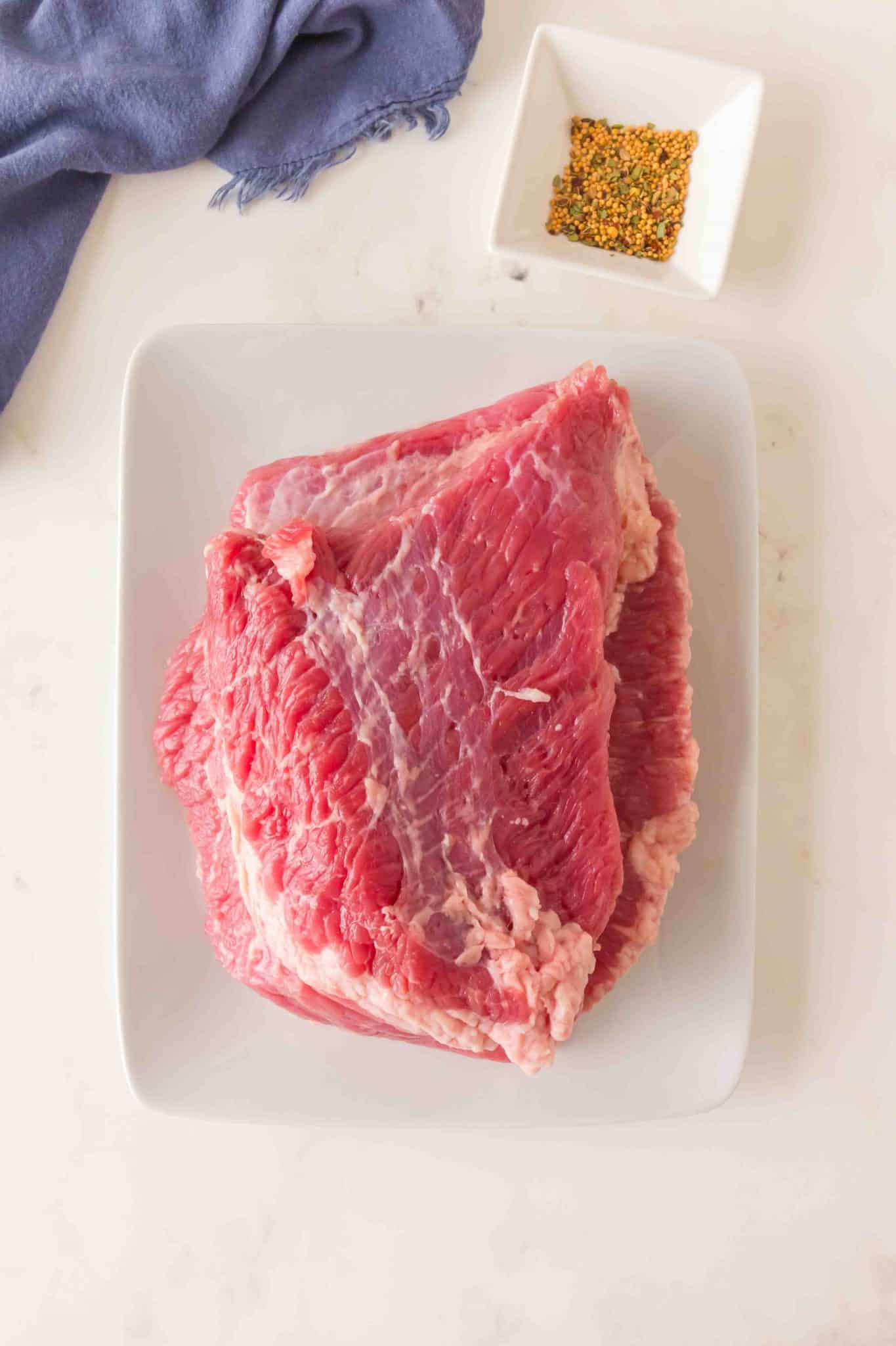 Top down view of the ingredients used to make oven-baked corned beef including the beef brisket and spices. Hostess At Heart