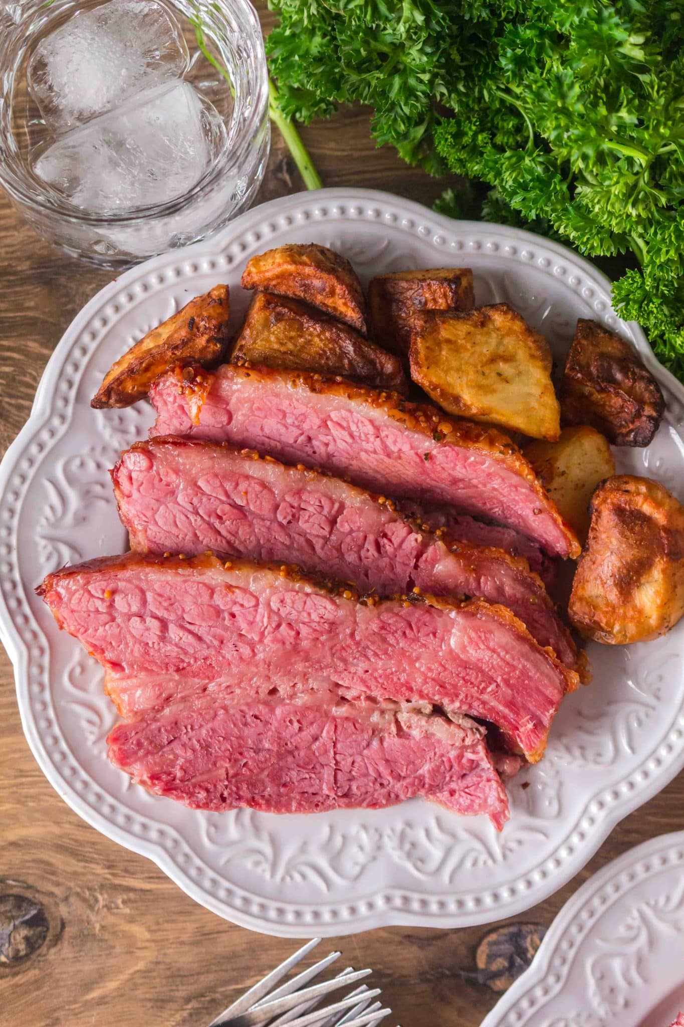 Top down view of a white plate filled with sliced oven-baked corned beef and roasted potatoes. Hostess At Heart