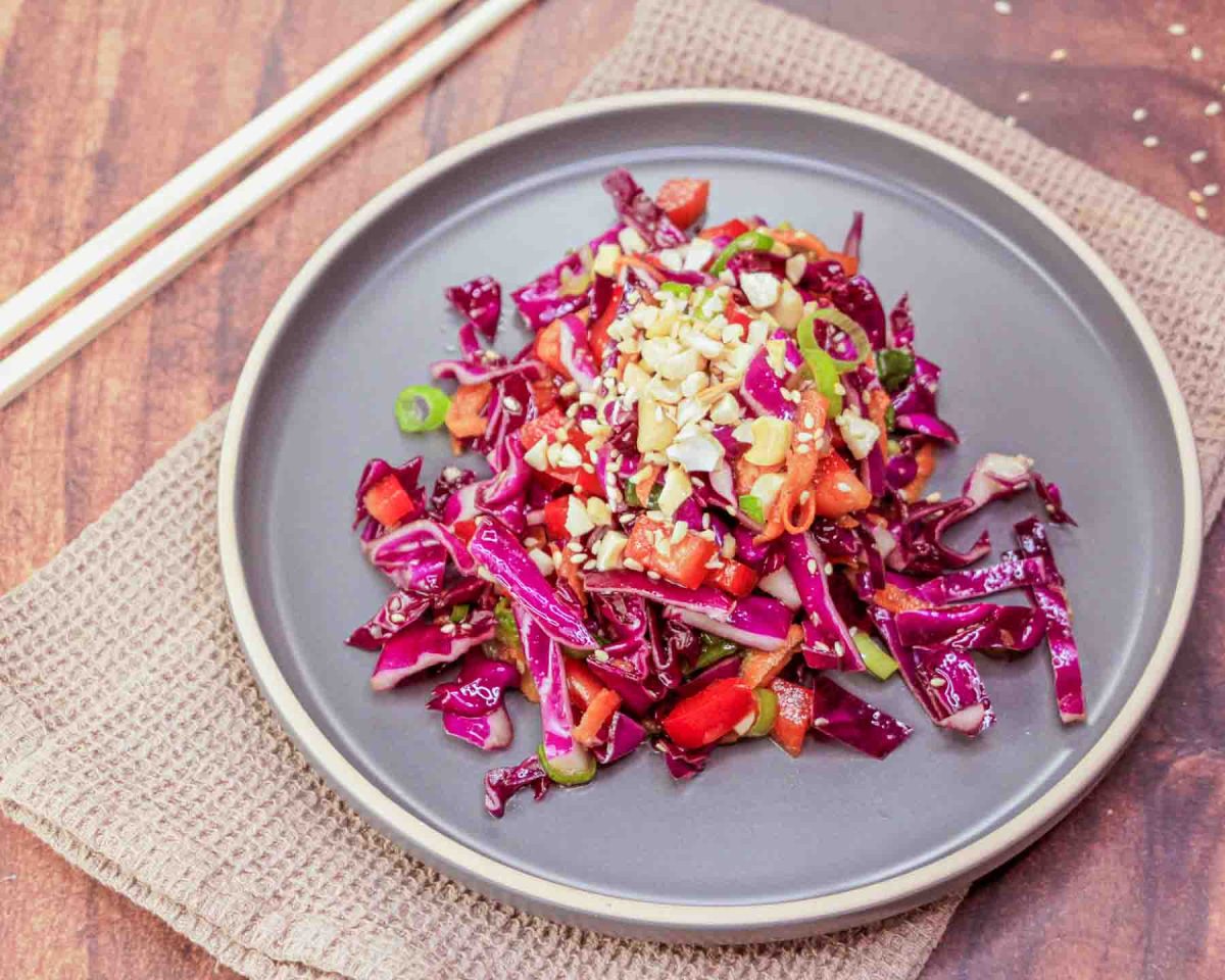 A plate filled with an Asian Cabbage Salad featuring raw red cabbage, peppers, carrots, in a ginger dressing garnished with cashews - Hostess At Heart