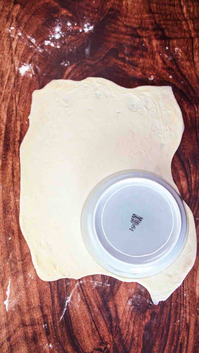 A dinner plate set on rolled pizza dough on a lightly floured surface. Hostess At Heart