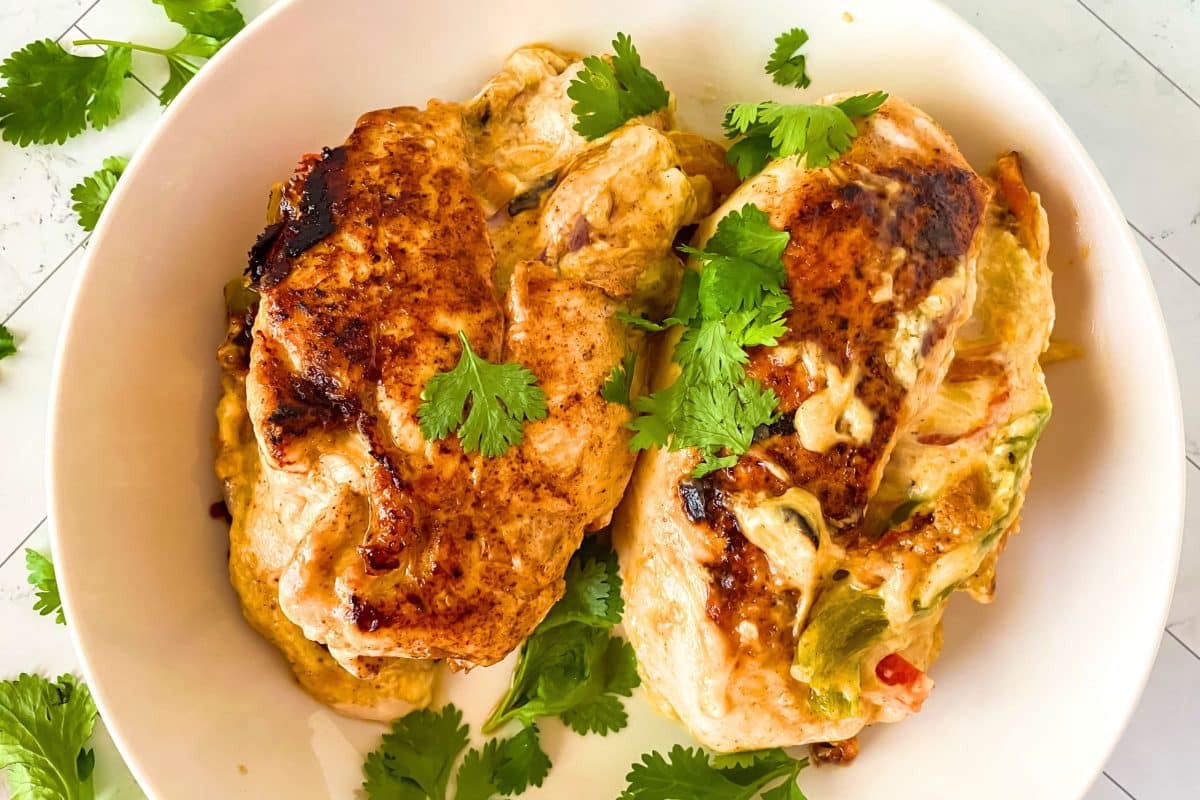 Top down view of two fajita seasoned baked stuffed chicken breasts in a serving dish garnished with cilantro - Hostess At Heart