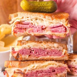 A stack of 3 traditional reuben sandwiches cut in half showing a thick layer of corned beef, creamy homemade thousand island dressing, juicy sauerkraut, and swiss cheese on rye bread. Hostess At Heart