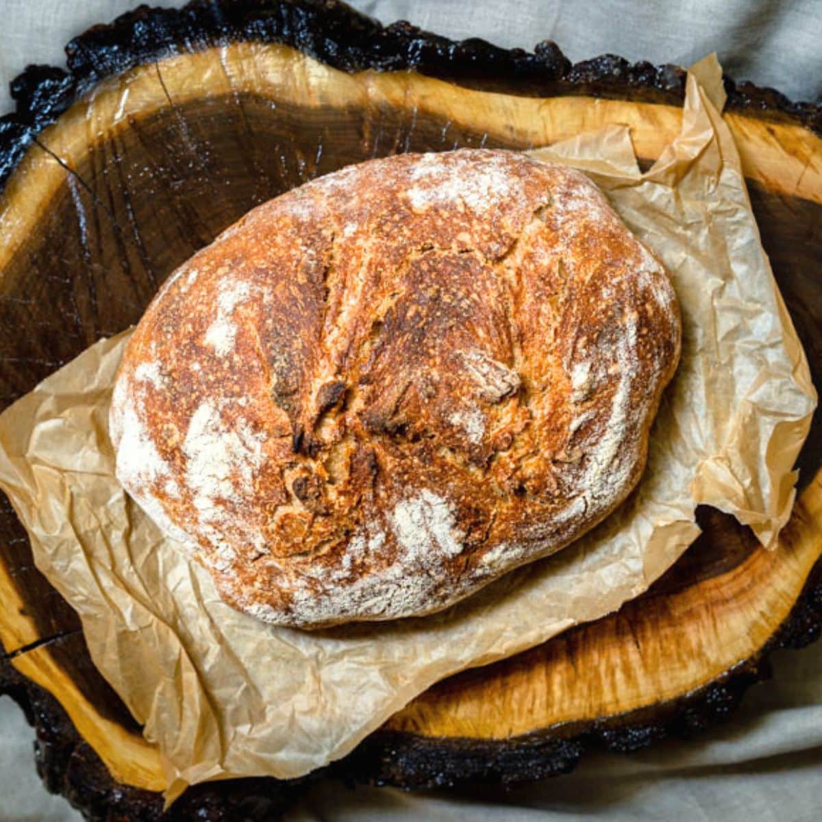 Top down view of a golden brown loaf os sourdough sitting on some rumpled parchment paper. Hostess At Heart