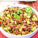 A titled image for Pinterest of Fresh avocado salsa with corn and black beans in a white bowl garnished with cilantro and sliced jalapenos. Hostess At Heart