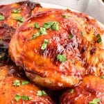 Close up of barbecued chicken thighs with sticky caramelized BBQ glaze garnished with fresh parsley. Hostess At Heart