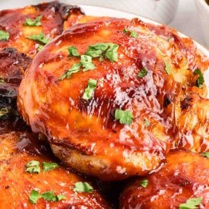 Close up of barbecued chicken thighs with sticky caramelized BBQ glaze garnished with fresh parsley. Hostess At Heart