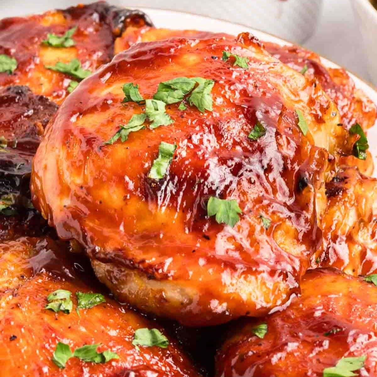 Close up of barbecued chicken thighs with sticky caramelized BBQ glaze garnished with fresh parsley. Hostess At Heart