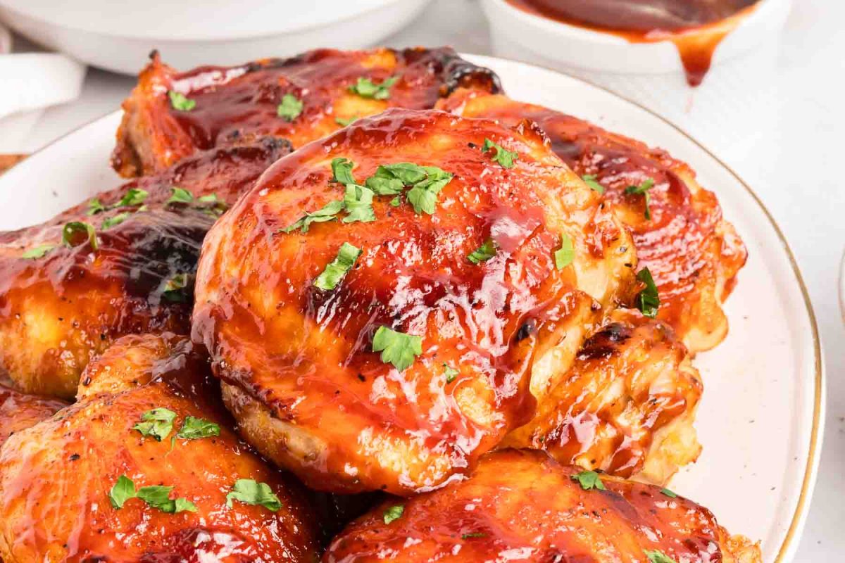 Close up of juicy baked chicken thighs on a platter with thick caramelized barbecue sauce. Hostess At Heart
