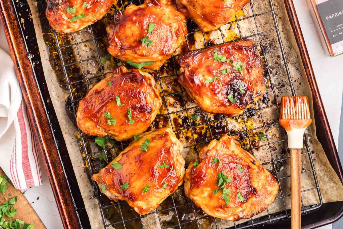 Oven Baked Barbecued chicken thighs on a rack after broiling with thick caramelized barbecue sauce glaze and garnished with parsley. Hostess At Heart