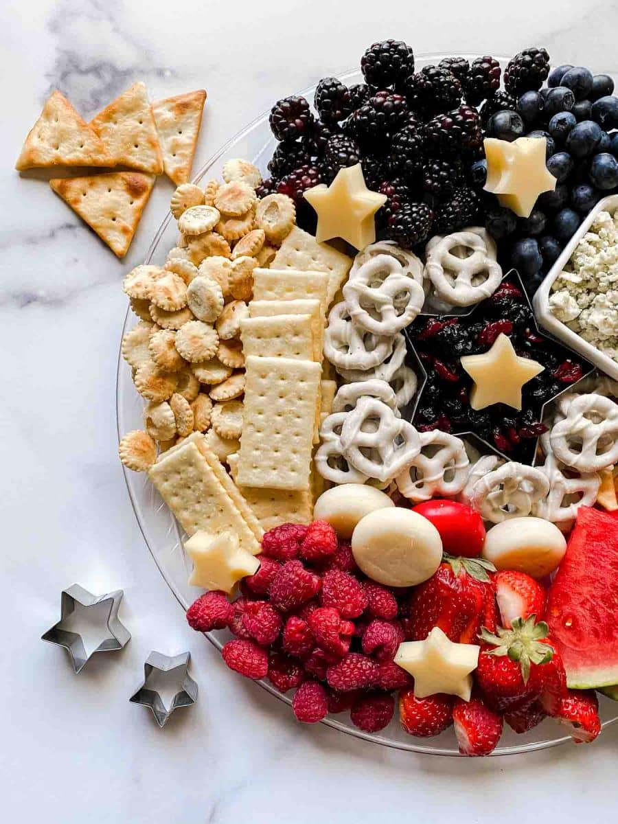 A tray filled with charcuterie board fruits, cheeses, crackers, pretzels, and dried fruit for Summer and Memorial Day entertaining. Hostess At Heart