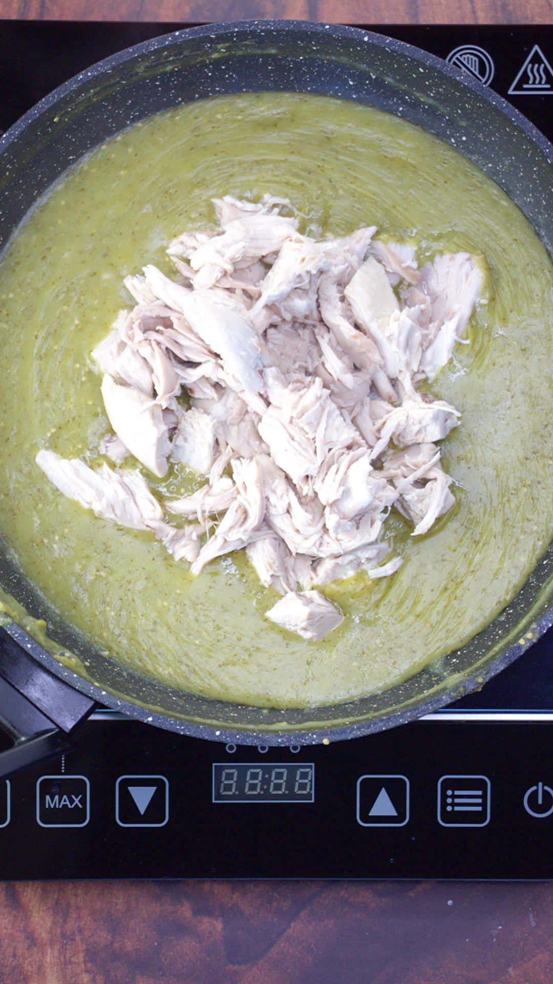 Shredded chicken being stirred into thick green mole sauce in a large saucepan. Hostess At Heart
