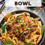 An image for Pinterest of Thai basil noodles in a dark bowl topped with sliced grilled chicken and garnished with green onions and fresh Thai basil. Hostess At Heart