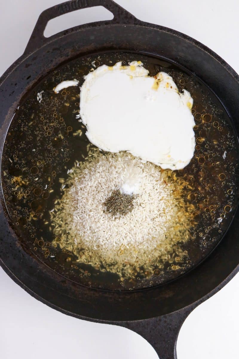 Long-grain rice, coconut milk, and chicken stock added to a cast iron skillet with spices. Hostess At Heart