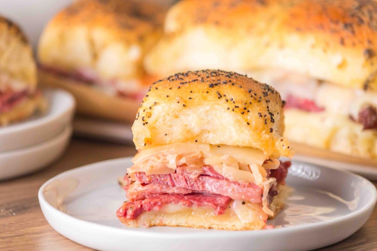 Close-up tableview of a corned beef slider on a Hawaiian roll layered with juicy corn beef and sauerkraut and topped with poppyseed butter baked into the top. Hostess At Heart